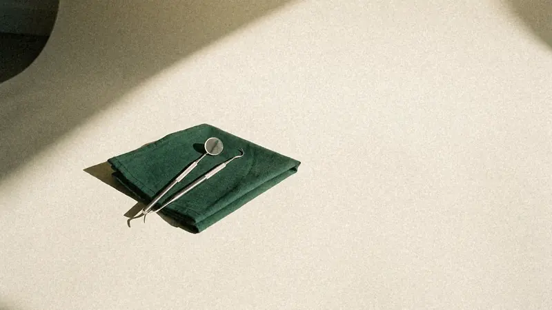 Katlanmış yeşil bez üzerinde diş hekimi aynası ve ince bir el aleti